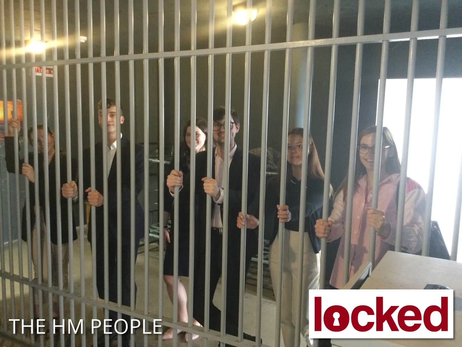 Smiling team members in an escape room, behind the bars of a cage