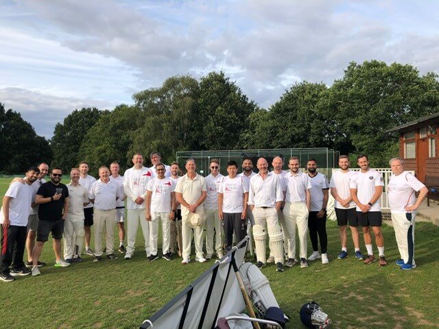Team members in cricket whites, standing on a cricket pitch
