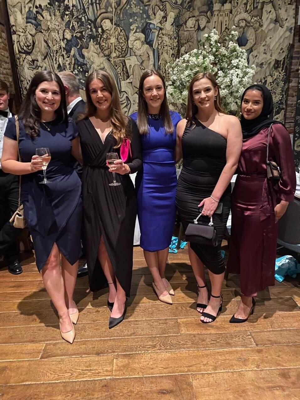 5 women in dresses holding wine glasses