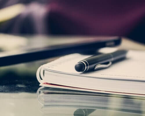 Close up picture of a pen and a notebook on a glass desk