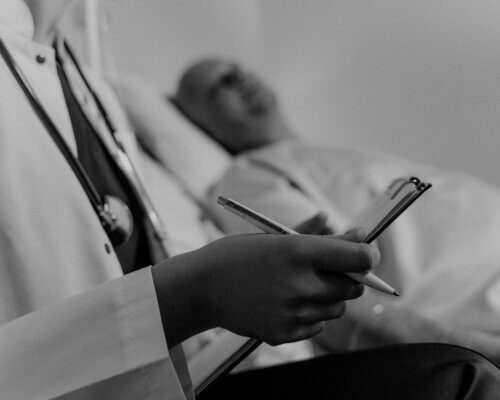 Picture of a doctor making notes on a patient in the background